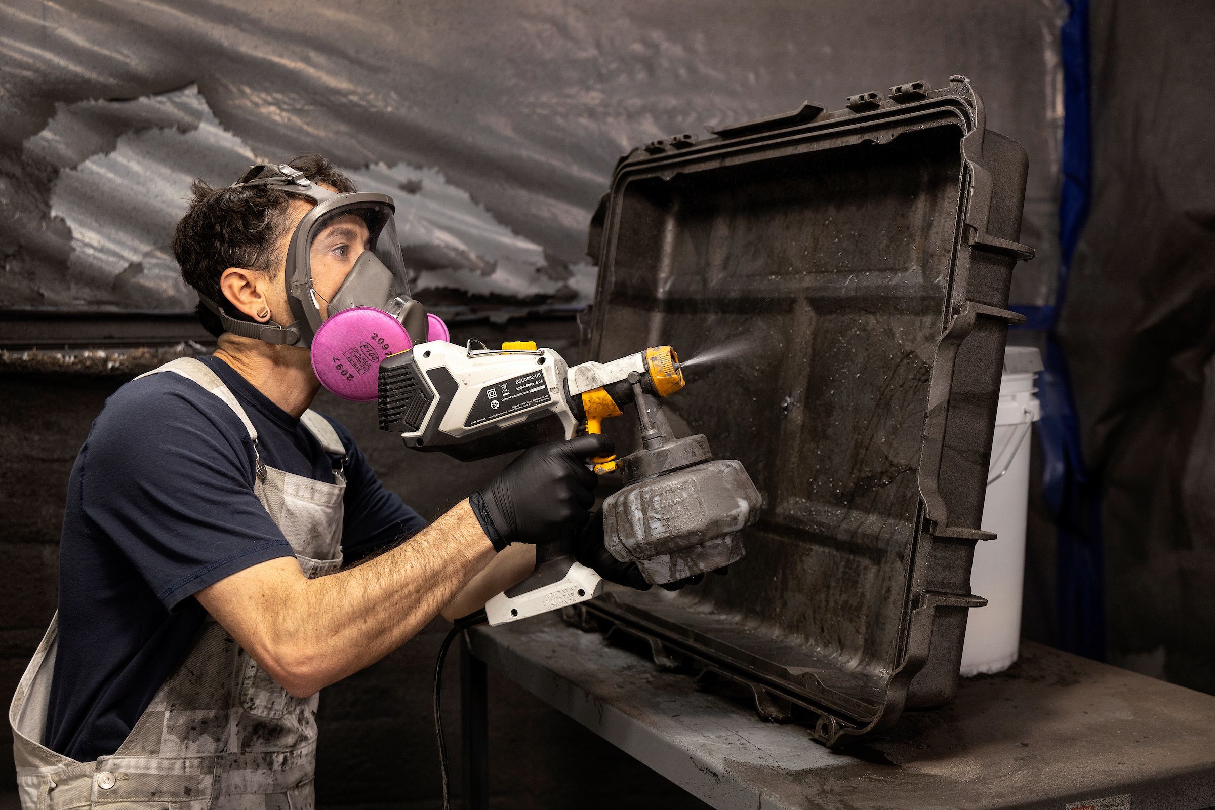 A technician in a respirator spray-applying conductive coating to a protective equipment case